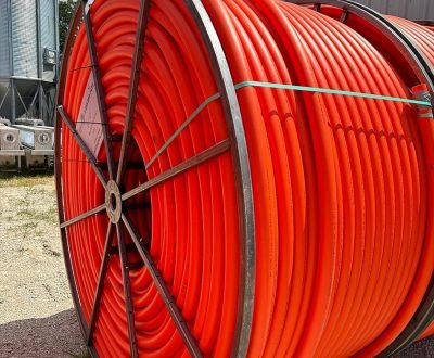 A standard orange HDPE conduit hose laying on the ground next to a silo.